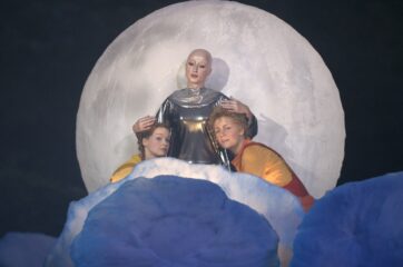 Aufführung der Oper "Hänsel und Gretel" im Schlosstheater 2005. änsel und Gretel knien vor einem riesigen Vollmond, personifiziert furch eine Darstellerin, die beide umarmt.