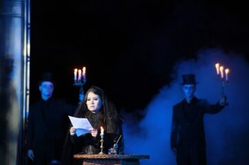 Dame in schwarz flankiert von zwei Fackelträgern bei der Aufführung von Eugen Onegin im Heckentheater 2009.