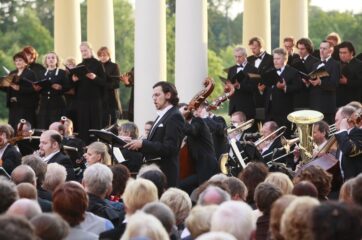 Konzert im Schlosshof während der Kammeroper 2009. Opernsänger umringt von Zuschauern und Orchester, im Hintergrund der Schlosspark.
